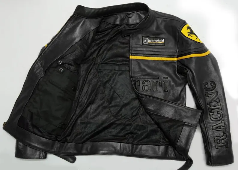 Close-up of a black vintage-style Ferrari Racing leather jacket with yellow stripe, Bell and Chesterfield patches, and embossed Racing text on the sleeves.
