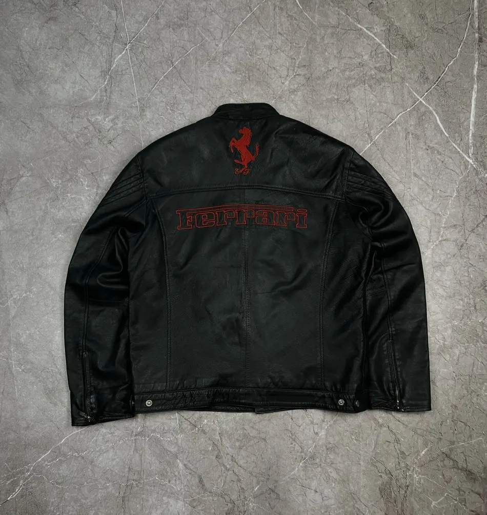 Full front view of a sleek black leather Ferrari jacket with red embroidered FERRARI text across the chest.